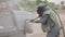 A man in a protective clothing and hard hat processes metal with a stream of sand. Worker in sandblasting uniform