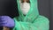 A man in a protective coat with a hood, a gauze mask and glasses on his face. He puts a rubber glove on his left hand and tucks a