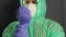 A man in a protective coat with a hood, a gauze mask and glasses on his face. He puts a rubber glove on his right hand and tucks a