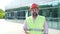 Man in protective helmet and vest makes report on construction site on street.