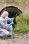 A man in a protective suit and mask performs an express test for water pollution from a river