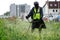 A man in a protective suit mows the grass with a handheld portable lawnmower. Improvement and economy of a big city