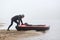 Man pulling canoe into water, wearing black clothing, posing on bank of river, handsome sports man doing water sport in foggy
