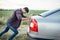 Man pushing broken car, side view