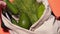 A man puts vegetables in a cotton bag on an isolated colored background. Cucumbers, tomatoes, avocados and other