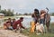 Man puts wood in fire. Group of people have picnic on the beach. Friends have fun at weekend time