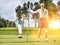 Man putting on green while female golfer holding the pin