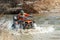 The man on the Quad bike rides on the river with a splashing water