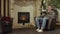 Man reading book near fireplace at home. Video. Middle aged man sitting in front of fireplace in his armchair at home on