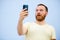 Man with a red beard looks into the phone with surprise and ecstasy a bright summer photo on a blue background