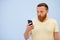 Man with a red beard looks into the phone with surprise and ecstasy a bright summer photo on a blue background