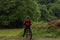 Man in red-black clothes on a bicycle in the woods. Thinking person on a mountain bike in the park. Trees in the background