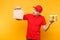 Man in red cap, t-shirt giving fast food order isolated on yellow background. Male employee courier hold paper packet