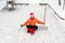 Man in a red Christmas hat and red winter boots in an orange sweater is sitting in a lotus position on the site of his yard with a