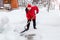 Man in red down jacket and red hat of Santa claus clears snow in backyard. Clears snowdrifts on path to home. In snowfall. Man