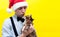 Man in red festive santa hat, blue shirt and black suspender holding and kissing cute brown tabby cat in front of yellow backgroun