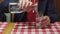 A man in a red hoodie and a blue jacket pours a glass of pure water from a jag bottle in an Italian restaurant. Visitor