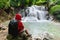 A man in red jacket with backpack sitting on the rock enjoying beautiful waterfall in tropical rain forest Huay Mae Khamin in Kanc