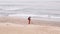 Man in red jumpsuit looking for the lost luxuries with electronic metal detector on the beach on a cloudy fall day. He