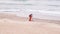 Man in red jumpsuit looking for lost luxuries with electronic metal detector on the beach on a cloudy fall day. He is