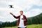 Man in a red shirt flies on a drone on a hike in the mountains  stands on a meadow with a remote control in his hands and looks at