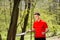 The man in a red t-shirt pose with a tennis racket and a ball on the background of green park. Sport concept