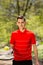 The man in a red t-shirt pose with a tennis racket and a ball on the background of green park. Sport concept