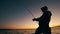 A man is reeling up a fishing pole in a sunset lake