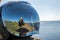 A man in the reflection of a motorcycle helmet sits on the seashore