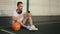 Man is relaxing on basketball court after training, using smartphone