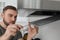 Man repairing modern cooker hood in kitchen, focus on hands