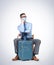 Man in a respiratory mask, glasses, a shirt and a tie sits with a suitcase waiting for a flight. Pandemic Travel concept.