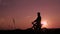 A man rides a bicycle on a hill at an orange sunset. Silhouette of a man on a bicycle. Look into the distance, travel the mountain