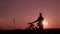 A man rides a bicycle on a hill at an orange sunset. Silhouette of a man on a bicycle. Look into the distance, travel the mountain