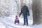 A man rides a little girl on a sled in the winter forest. Grandfather takes his granddaughter on a sled through a snow-covered