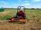 A man rides a tractor with a mower in a field. Mulching and mowing the grass. Clear day, blue sky. Land cultivation