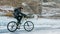 Man is riding bicycle near ice grotto. Rock with ice caves icicl