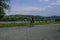 A man riding a bike on the bike lane across the mountains view, river and a bridge over the river. Langhirano, Italy