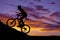 Man riding a bike up a hill silhouette in the sunset