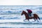 Man riding on a brown galloping horse in the sea waters of Ayia Erini beach in Cyprus against a rough sea