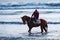 Man riding on a brown galloping horse in the sea waters of Ayia Erini beach in Cyprus against a rough sea