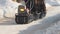 Man riding on crawler mini snowmobile with a trailer and a passenger on a winter road