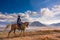 A man riding a horse with Mount Batok in the background