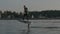 Man riding on a hydrofoil surfboard near lake shore and marina at golden sunset