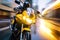 a man riding a yellow motorcycle down a street next to a tall building with a clock on the front of it\\\'s headlight