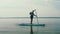 A man rises from his knees on a SUP board in the lake with a paddle