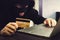 Man in robber mask and hood misappropriates personal bank data. Cyber fraudster attacks online banking system. Hacker