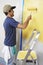 Man With Roller Applying Yellow Paint On A Wall