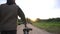 A man rolls a bicycle along a gravel country road against the backdrop of a sunny sunset. Beautiful nature and field