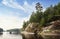 man rows on boat in nordic rocky bay. Big slanted pine on granite cliff. Baltic sea, gulf of Finland